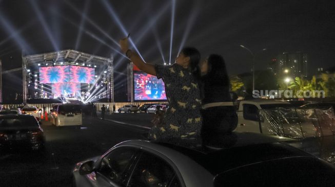 Dua orang penonton berswafoto dari atap mobilnya saat gelaran konser drive-in di Jiexpo Kemayoran, Jakarta Pusat, Minggu (30/8). [Suara.com/Alfian Winanto]