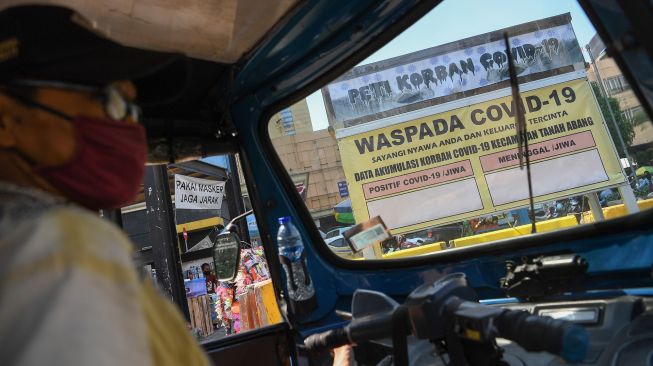 Seorang sopir bajaj menunggu penumpang dengan latar belakang replika peti mati dan papan himbauan waspada COVID-19 di kawasan Pasar Tanah Abang, Jakarta, Selasa (1/9/2020). [ANTARA FOTO/ Wahyu Putro] 