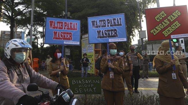 Sejumlah Aparatur Sipil Negara (ASN) membawa poster imbauan saat peresmian simbol peringatan COVID-19 di Simpang Lima Senen, Jakarta, Selasa (1/9/2020). [Suara.com/Angga Budhiyanto]