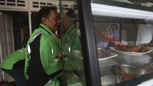 Petugas melayani pengemudi ojek onlne yang akan menikmati hidangan makan gratis di Warung Makan Rakyat, Beji, Depok, Jawa Barat, Kamis (3/9/2020). [Suara.com/Angga Budhiyanto]