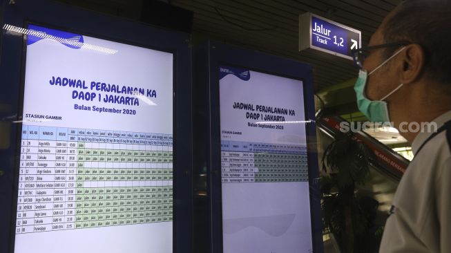 Seorang calon penumpang melihat papan informasi jadwal perjalanan kereta api di Stasiun Gambir, Jakarta, Kamis (3/9/2020). [Suara.com/Angga Budhiyanto]