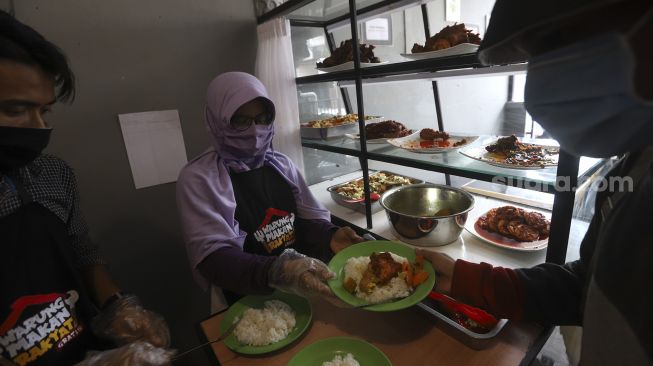 Petugas melayani warga yang akan menikmati hidangan makan gratis di Warung Makan Rakyat, Beji, Depok, Jawa Barat, Kamis (3/9/2020). [Suara.com/Angga Budhiyanto]