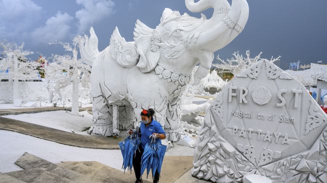 Seorang karyawan membawa payung di antara patung-patung mitos yang terbuat dari pasir putih yang menyerupai es di taman "Frost Magical Ice of Siam" di luar Pattaya, Thailand (2/9/2020). [Mladen ANTONOV / AFP]