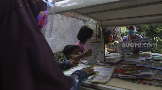 Sejumlah anak membaca buku koleksi dari Bemo Baca milik Sutino (60) bertepatan dengan Hari Aksara Internasional (HAI) di Jakarta, Selasa (8/9/2020). [Suara.com/Angga Budhiyanto]