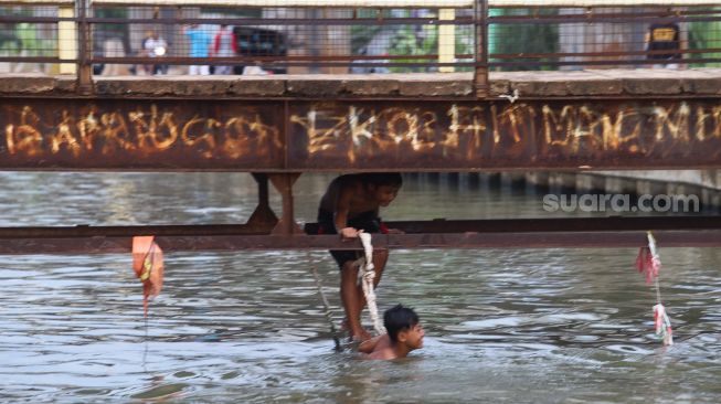 Anak - anak bermain air dibawah jembatan saat berenang di saluran Kalimalang, Kalimalang, Jakarta Timur, Selasa (15/9). [Suara.com/Alfian Winanto]