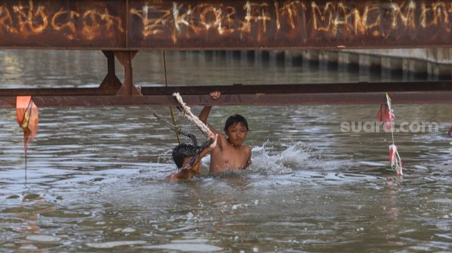 Anak - anak bermain air saat berenang di saluran Kalimalang, Kalimalang, Jakarta Timur, Selasa (15/9). [Suara.com/Alfian Winanto]