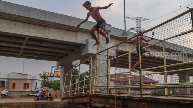 Seorang anak melompat dari atas pagar jembatan saat berenang di saluran Kalimalang, Kalimalang, Jakarta Timur, Selasa (15/9). [Suara.com/Alfian Winanto]