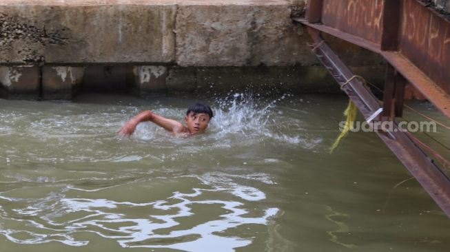 Seorang anak berenang di saluran Kalimalang, Kalimalang, Jakarta Timur, Selasa (15/9). [Suara.com/Alfian Winanto]