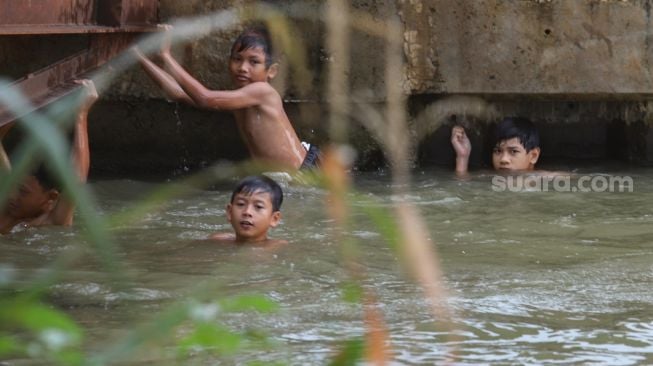 Anak - anak berenang di saluran Kalimalang, Kalimalang, Jakarta Timur, Selasa (15/9). [Suara.com/Alfian Winanto]