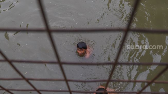 Anak - anak berenang dibawah jembatan di saluran Kalimalang, Kalimalang, Jakarta Timur, Selasa (15/9). [Suara.com/Alfian Winanto]