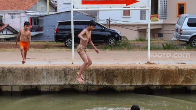 Anak - anak melompat ke dalam air saat berenang di saluran Kalimalang, Kalimalang, Jakarta Timur, Selasa (15/9). [Suara.com/Alfian Winanto]