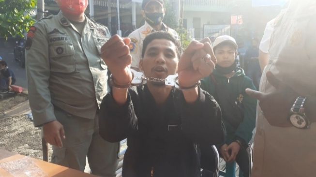 Seorang pengendara roda dua bernama Andi Albar saat memperlihatkan tangannya di borgol karena tidak mengguna masker di Jalan Raya Puncak Bogor Jawa Barat. (Suara.com/Andi Ahmad Sulaendi).
