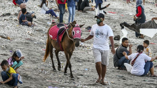 Warga menuntun kudanya yang disewakan di pesisir pantai batu-batu Kenjeran, Surabaya, Jawa Timur, Minggu (20/9/2020). [ANTARA FOTO/M Risyal Hidayat]