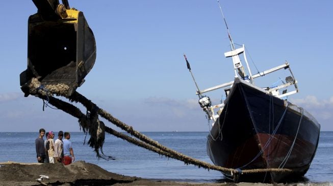 Pekerja melihat kapal nelayan yang ditarik ke atas daratan menggunakan alat berat sebelum diperbaiki di Pantai Batu-Batu, Kabupaten Takalar, Sulawesi Selatan, Senin (21/9/2020). [ANTARA FOTO/Arnas Padda]