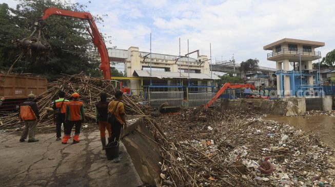 Petugas UPK Badan Air Dinas Lingkungan Hidup Provinsi DKI Jakarta dibantu alat berat mengangkat sampah kayu yang menumpuk di pintu air Manggarai, Jakarta, Selasa (22/9/2020). [Suara.com/Angga Budhiyanto]