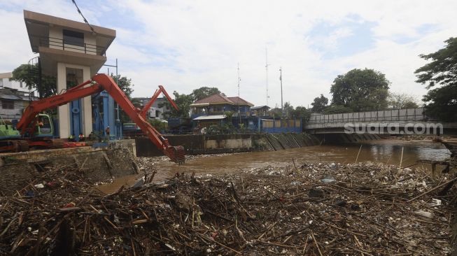 Petugas UPK Badan Air Dinas Lingkungan Hidup Provinsi DKI Jakarta dibantu alat berat mengangkat sampah kayu yang menumpuk di pintu air Manggarai, Jakarta, Selasa (22/9/2020). [Suara.com/Angga Budhiyanto]