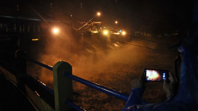 Pengendara motor melintas di atas jembatan sungai Warga memotret derasnya debit air sungai Ciliwung di Bendung Katulampa, Kota Bogor, Jawa Barat, Senin (21/9/2020).  [ANTARA FOTO/Arif Firmansyah]