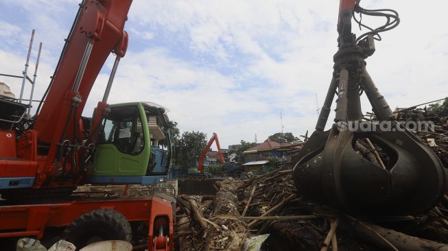 Petugas UPK Badan Air Dinas Lingkungan Hidup Provinsi DKI Jakarta dibantu alat berat mengangkat sampah kayu yang menumpuk di pintu air Manggarai, Jakarta, Selasa (22/9/2020). [Suara.com/Angga Budhiyanto]