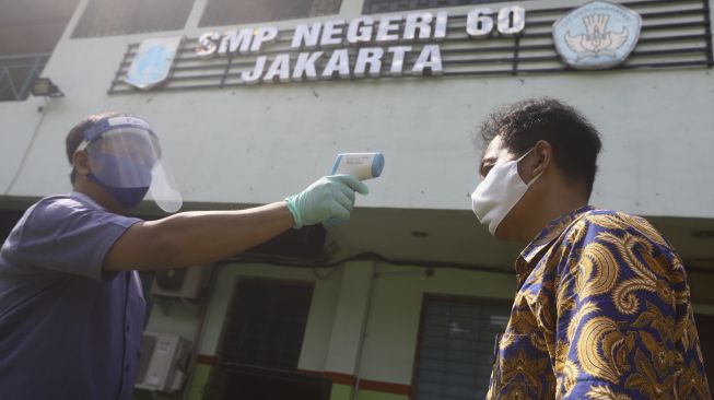 Petugas memindai suhu tubuh seorang tamu dalam simulasi pendaftaran di posko PPDB SMP Negeri 60, Kecamatan Gambir, Jakarta Pusat, Rabu (10/6/2020). [Suara.com/Angga Budhiyanto]