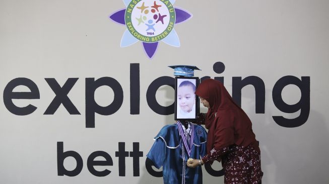 Kepala Sekolah mengalungkan piagam tanda kelulusan kepada siswa Kelompok Bermain Taman Kanak-kanak (KB TK) saat wisuda virtual menggunakan Roboda (Robot Wisuda) di Sekolah Nasional Satu (Nassa School), Bekasi, Jawa Barat, Rabu (1/7/2020) . [Suara.com/Angga Budhiyanto]