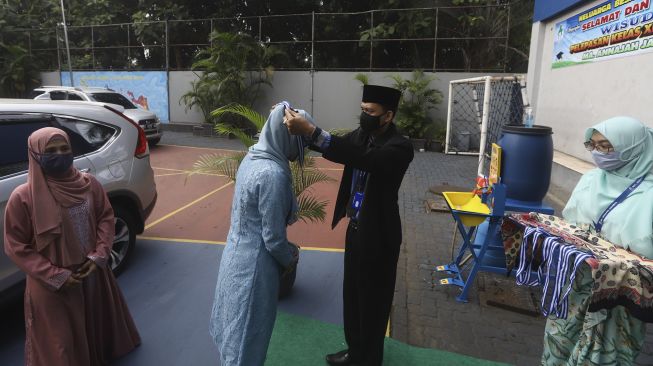 Seorang murid disaksikan orang tua menerima pengalungan medali dari guru sebagai tanda wisuda kelulusan sekolah secara "Drive Thru" di Madrasah Aliyah Annajah, Ciledug Raya, Jakarta, Jumat (19/6). [Suara.com/Angga Budhiyanto]