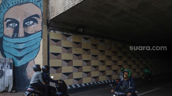 Warga melintas didepan mural Covid-19 bergambar tenaga medis di Terowongan Stasiun Cawang, Tebet, Jakarta Selatan, Senin (28/9). [Suara.com/Alfian Winanto]