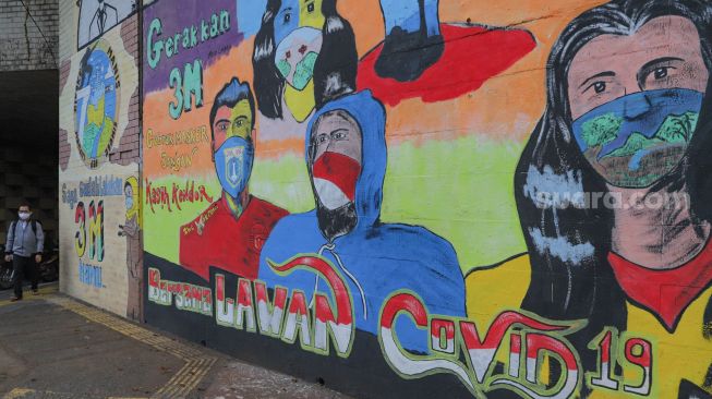 Warga melintas didepan mural Covid-19 yang menghias dinding di Terowongan Stasiun Cawang, Tebet, Jakarta Selatan, Senin (28/9). [Suara.com/Alfian Winanto]