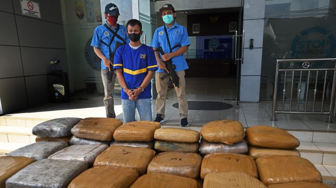 Petugas Badan Narkotika Nasional (BNN) Provinsi Banten menunjukkan AS (32) tersangka penyelundup ganja dari Aceh beserta barang bukti saat rilis kasus di Serang, Banten, Rabu (30/9/2020). [ANTARA FOTO/Asep Fathulrahman]