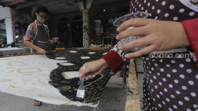 Restu Rizky Ramadhan (13) dibantu Ibunya menyelesaikan proses pembuatan motif batik di Rumah Batik Palbatu, Jakarta, Jumat (2/10/2020). [Suara.com/Angga Budhiyanto]