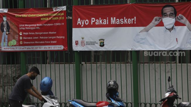 Seorang pengendara motor memarkirkan motornya di depan spanduk imbauan menggunakan masker di kawasan MH Thamrin, Jakarta, Jumat (2/10/2020). [Suara.com/Angga Budiyanto]