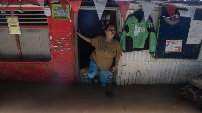 Seorang ibu berdiri di depan rumahnya yang terendam banjir di kawasan permukiman Petogogan, Kebayoran Baru, Jakarta Selatan, Senin (5/10/2020). [ANTARA FOTO/Sigid Kurniawan]