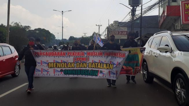 Ratusan buruh tergabung dalam organisasi PPMI menggelar aksi longmarch di Jalan Jakarta-Bogor, Selasa (6/10/2020). [Suara.com/Andi Ahmad Sulaendi]