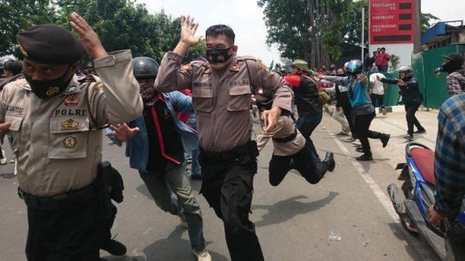 Anggota kepolisian berlari saat massa menerobos barikade di Jalan Daan Mogot, Jakarta Barat, Kamis (8/10).  [Suara.com/ Irfan Maulana]