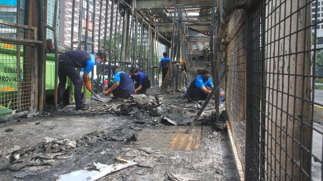 Sejumlah petugas membersihkan puing Halte Bus Trans-Jakarta Tosari yang hangus saat kericuhan unjuk rasa menolak pengesahan Undang-Undang Cipta Kerja di Jalan MH. Thamrin, Jakarta, Jumat (9/10/2020). [Suara.com/Oke Atmaja]