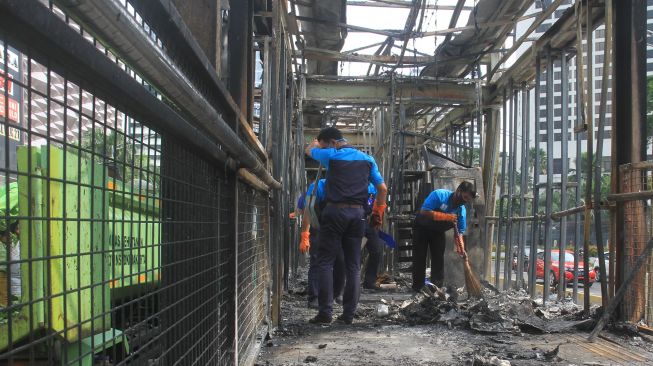 Sejumlah petugas membersihkan puing Halte Bus Trans-Jakarta Tosari yang hangus saat kericuhan unjuk rasa menolak pengesahan Undang-Undang Cipta Kerja di Jalan MH. Thamrin, Jakarta, Jumat (9/10/2020). [Suara.com/Oke Atmaja]