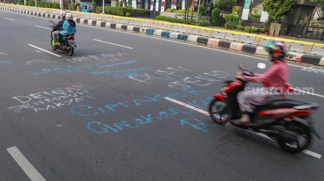 Warga melintas dijalan Ridwan Rais yang masih dipenuhi coretan aksi demo tolak Omnibus Law Kamis lalu di Jakarta Pusat, Sabtu (10/10). [Suara.com/Alfian Winanto]