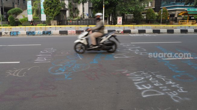 Warga melintas dijalan Ridwan Rais yang masih dipenuhi coretan aksi demo tolak Omnibus Law Kamis lalu di Jakarta Pusat, Sabtu (10/10). [Suara.com/Alfian Winanto]