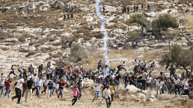 Pengunjuk rasa Palestina berlarian di tengah asap gas air mata selama bentrokan dengan pasukan keamanan Israel di dekat desa Beit Dajan, Palestina, pada (9/10/2020). [JAAFAR ASHTIYEH / AFP]