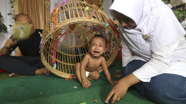 Seorang bayi dimasukkan ke dalam kurungan pada prosesi tradisi Tedak Siten di Kota Kediri, Jawa Timur, Minggu (11/10/2020). [ANTARA FOTO/Prasetia Fauzani