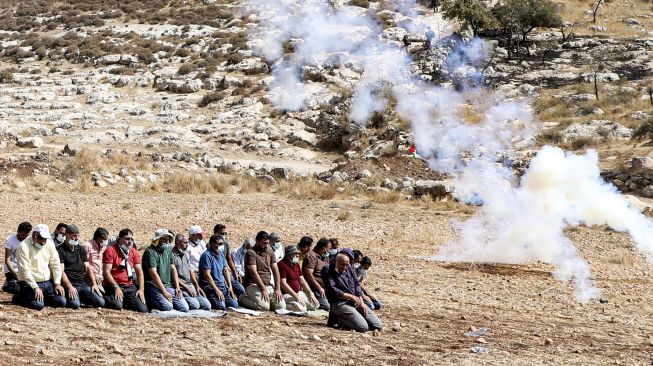 Pengunjuk rasa Palestina berdoa di tengah asap gas air mata yang ditembakkan oleh pasukan keamanan Israel di dekat desa Beit Dajan, Palestina, pada (9/10/2020). [JAAFAR ASHTIYEH / AFP]