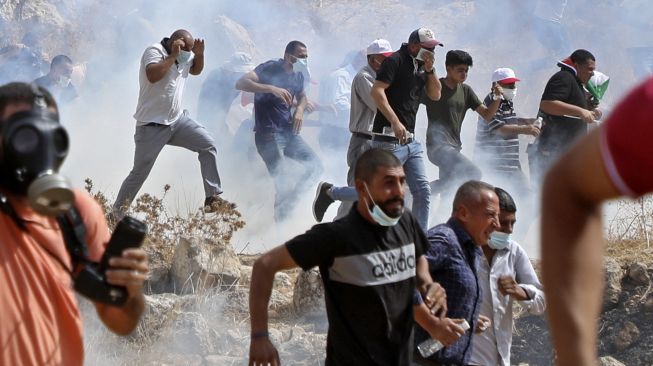 Pengunjuk rasa Palestina berlarian di tengah asap gas air mata selama bentrokan dengan pasukan keamanan Israel di dekat desa Beit Dajan, Palestina, pada (9/10/2020). [JAAFAR ASHTIYEH / AFP]