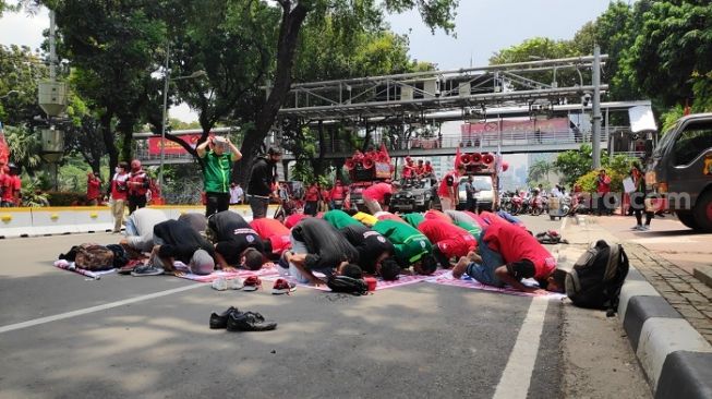 Sejumlah buruh dari KSBSI menggelar salat Zuhur berjemaah di tengah aksi di dekat Istana. (Suara.com/Bagaskara)