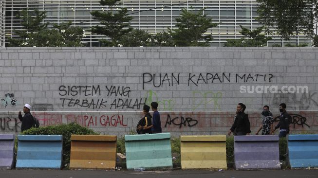 Sejumlah massa melintas di depan coretan berisi kritik kepada Dewan Perwakilan Rakyat di Kedutaan Besar Amerika Serikat, Jakarta, Selasa (13/10/2020). [Suara.com/Angga Budhiyanto]