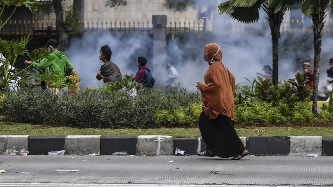 Seorang wanita berlari saat terjadi bentrokan antara petugas kepolisian dengan massa aksi tolak UU Cipta Kerja di kawasan jalan MH Thamrin, Jakarta, Selasa (13/10/2020).  [ANTARA FOTO/Muhammad Adimaja]