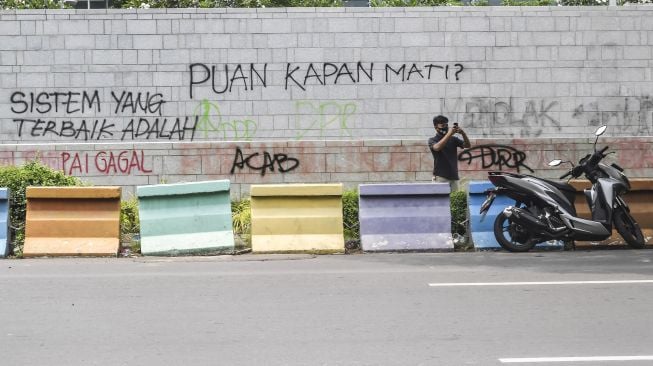 Warga berswafoto dengan latar belakang tembok yang dicoret-coret oleh orang tidak bertanggungjawab saat aksi Tolak UU Cipta Kerja di depan Kedutaan Amerika Serikat, Jakarta, Rabu (14/10/2020). [ANTARA FOTO/Muhammad Adimaja]