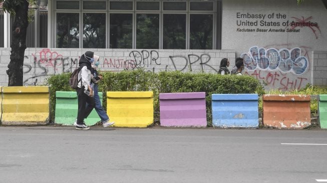 Warga berjalan di depan tembok yang dicoret-coret oleh orang tidak bertanggungjawab saat aksi Tolak UU Cipta Kerja di depan Kedutaan Besar Amerika Serikat, Jakarta, Rabu (14/10/2020).  [ANTARA FOTO/Muhammad Adimaja]