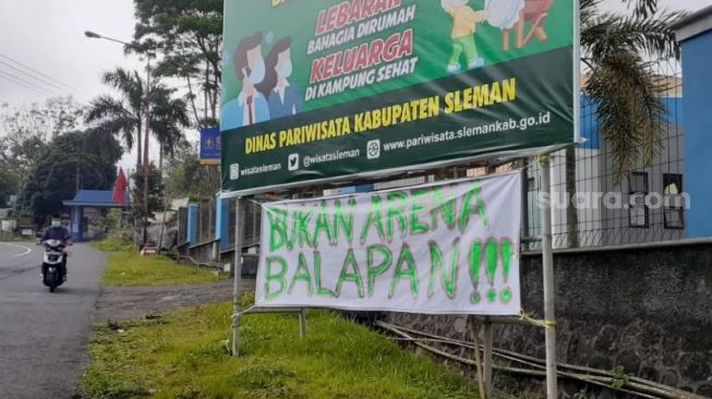 Pengendara motor melintasi spanduk peringatan untuk pembalap liar yang terpasang di Jalan Kaliurang KM 23, Pedukuhan Ngipiksari Kalurahan Hargobinangun, Kapanewon Pakem, Sleman, Jumat (16/10/2020). - (SuaraJogja.id/Muhammad Ilham Baktora)