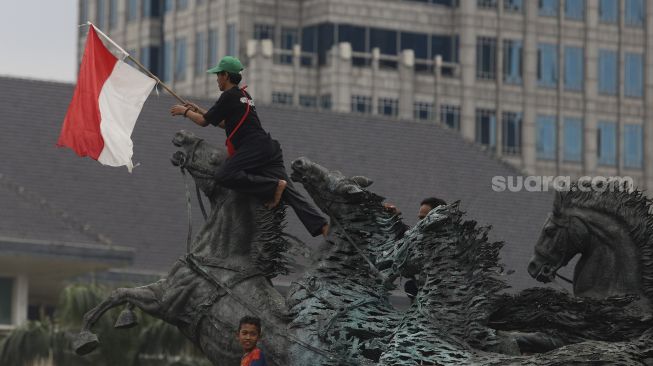 Massa aksi membawa bendera Merah Putih menaiki Patung Kuda saat melakukan aksi unjuk rasa di Jakarta, Selasa (20/10/2020). [Suara.com/Angga Budhiyanto]