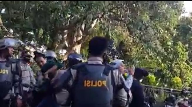 Capture a viral video screen of plainclothes police officers attacking Brimob members when they arrest a man suspected of being a student in connection with a demonstration against the Ciptaker Act in Jambi.  (Twitter)