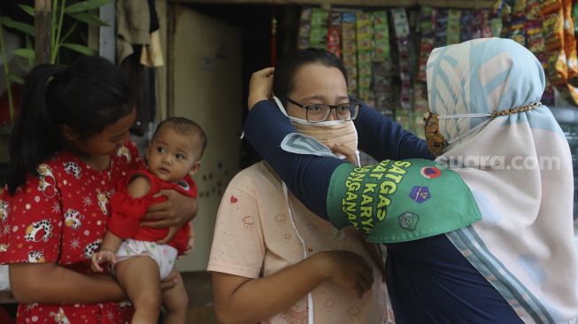 Satgas Padat Karya Penanganan COVID-19 Kelurahan Pejaten Barat memasangkan masker kepada warga saat sosialisasi protokol kesehatan di Kelurahan Pejaten Barat, Pasar Minggu, Jakarta, Kamis (22/10/2020). [Suara.com/Angga Budhiyanto]